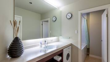 A modern bathroom with a sink, mirror, clock, and a washing machine.