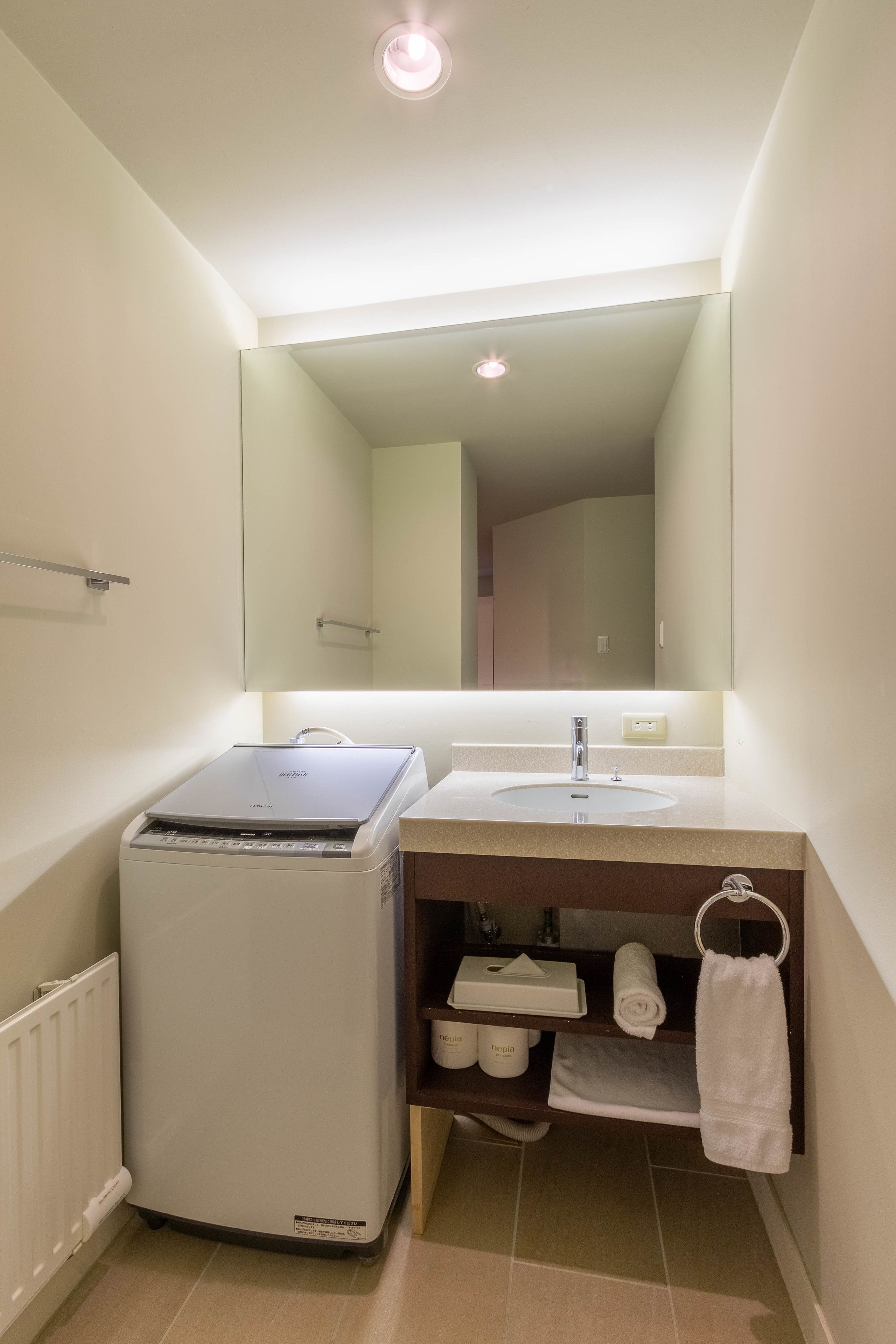 A compact bathroom with a built-in washing machine, a sink, and a mirror above it.