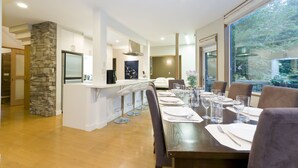 A modern kitchen with a central island, bar stools, and a dining area with a long table set for six. - Furano Fresh Powder Apartments and Chalet (Furano)