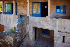 A stone building with multiple rooms, each with a blue door and window frames. - As Chivas (Redondela)
