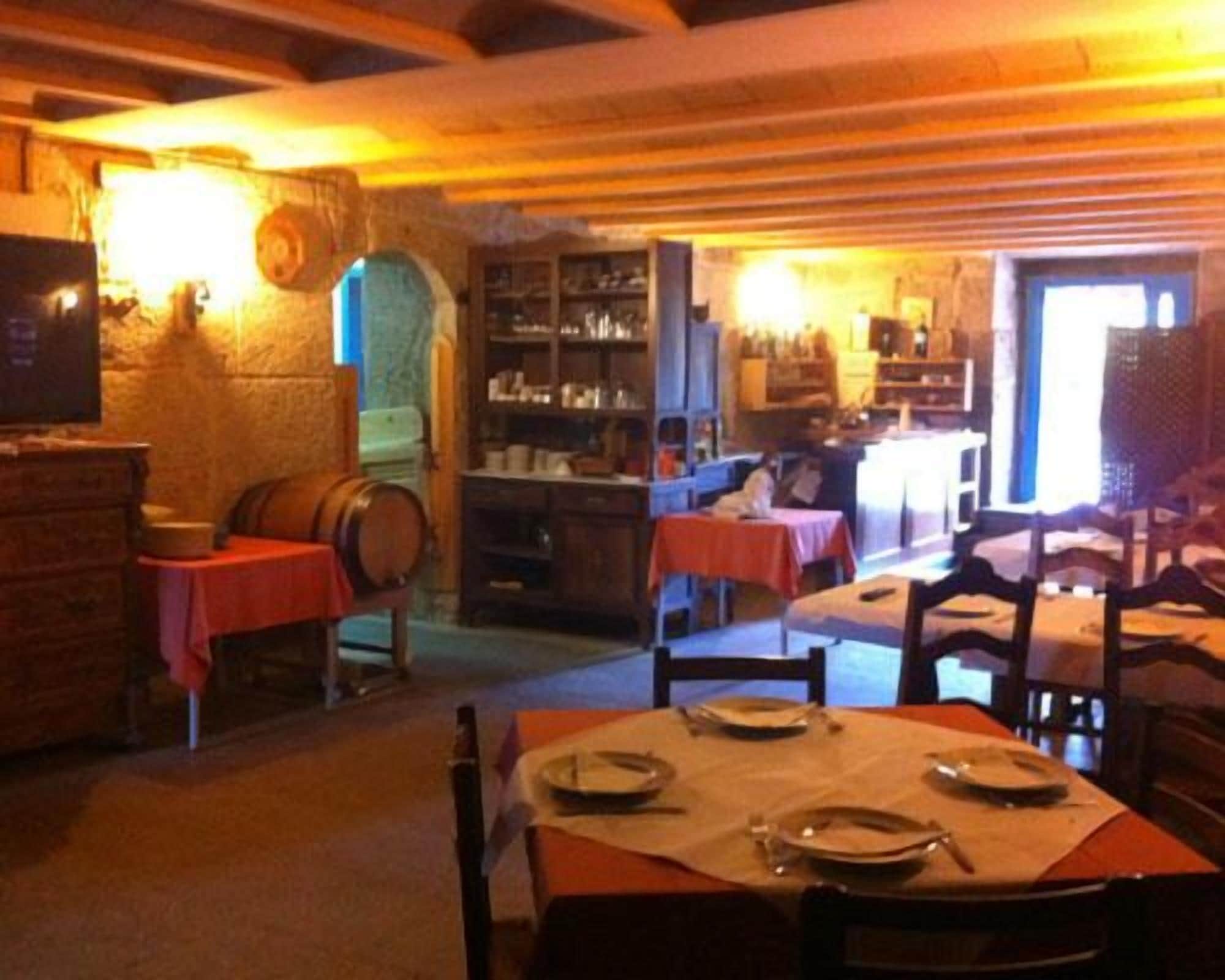 A rustic dining area with wooden tables and chairs, a stone wall, and a bookshelf filled with books and decorative items.