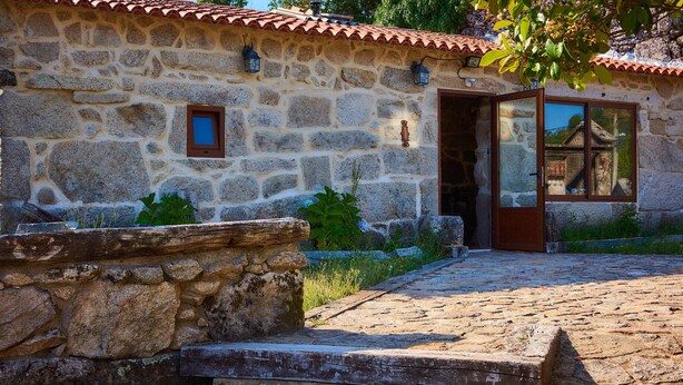 Un edificio in pietra con tetto in tegole, una panca in legno e una scalinata in pietra che porta a una porta.