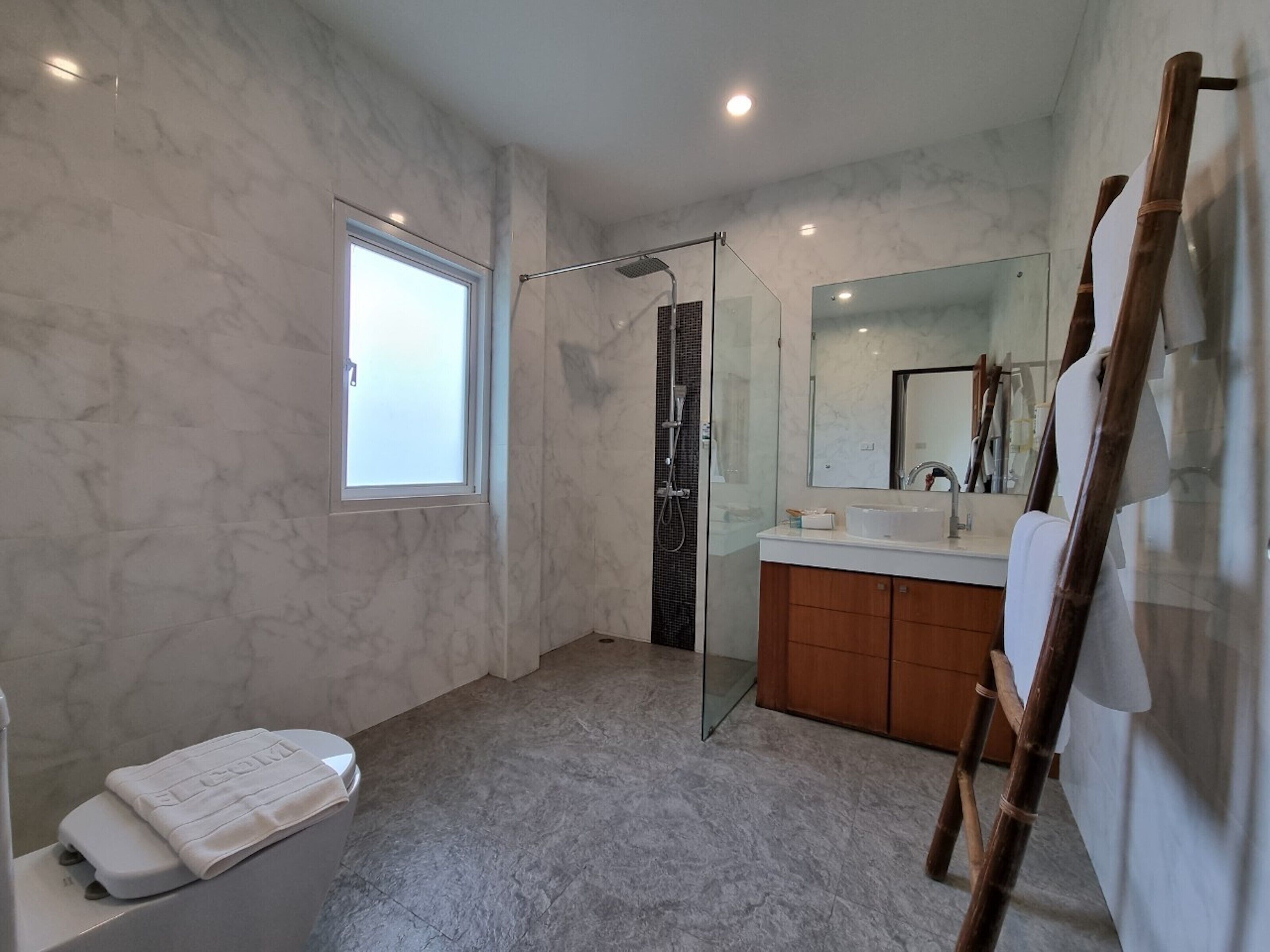 Een moderne badkamer met een douchecabine van glas, een grote spiegel en een houten ladder tegen de muur.