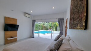 Un dormitorio con una cama grande, un televisor de pantalla plana montado en la pared y vistas a una piscina a través de puertas de cristal.