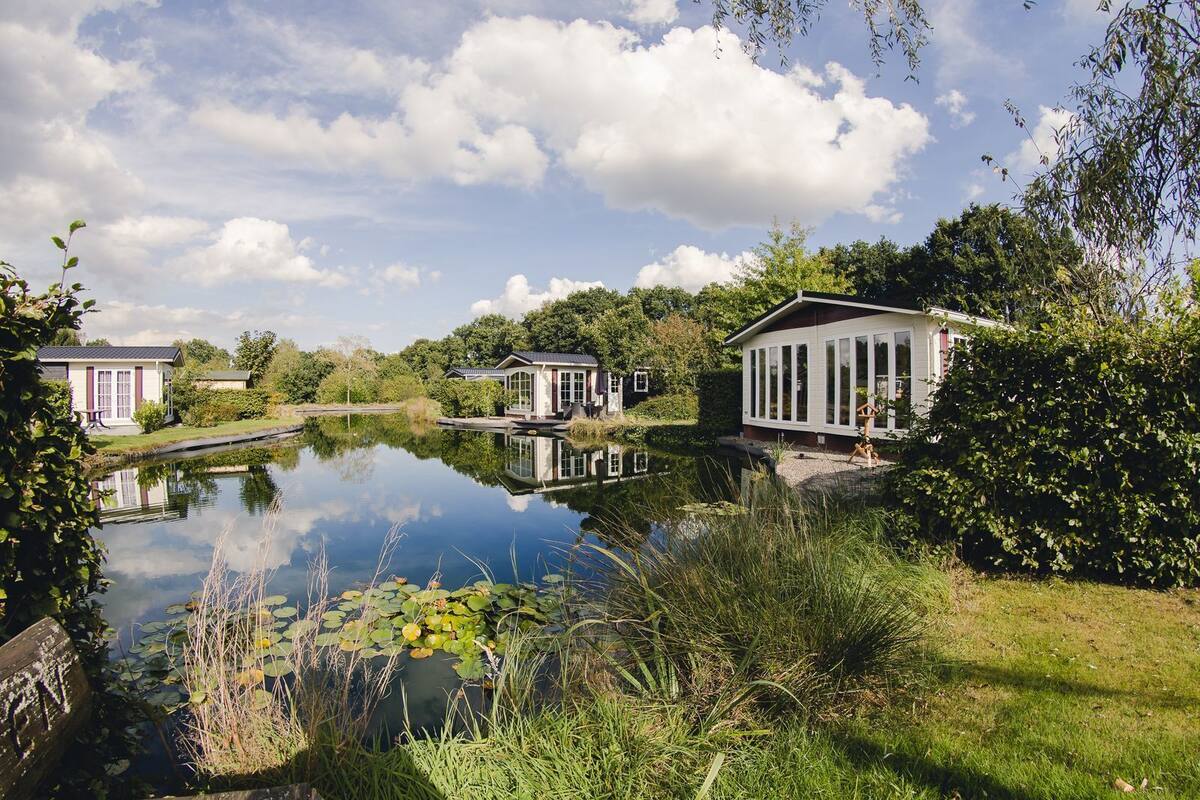 A serene lakeside setting with three distinct buildings, each featuring large windows and a modern architectural style.