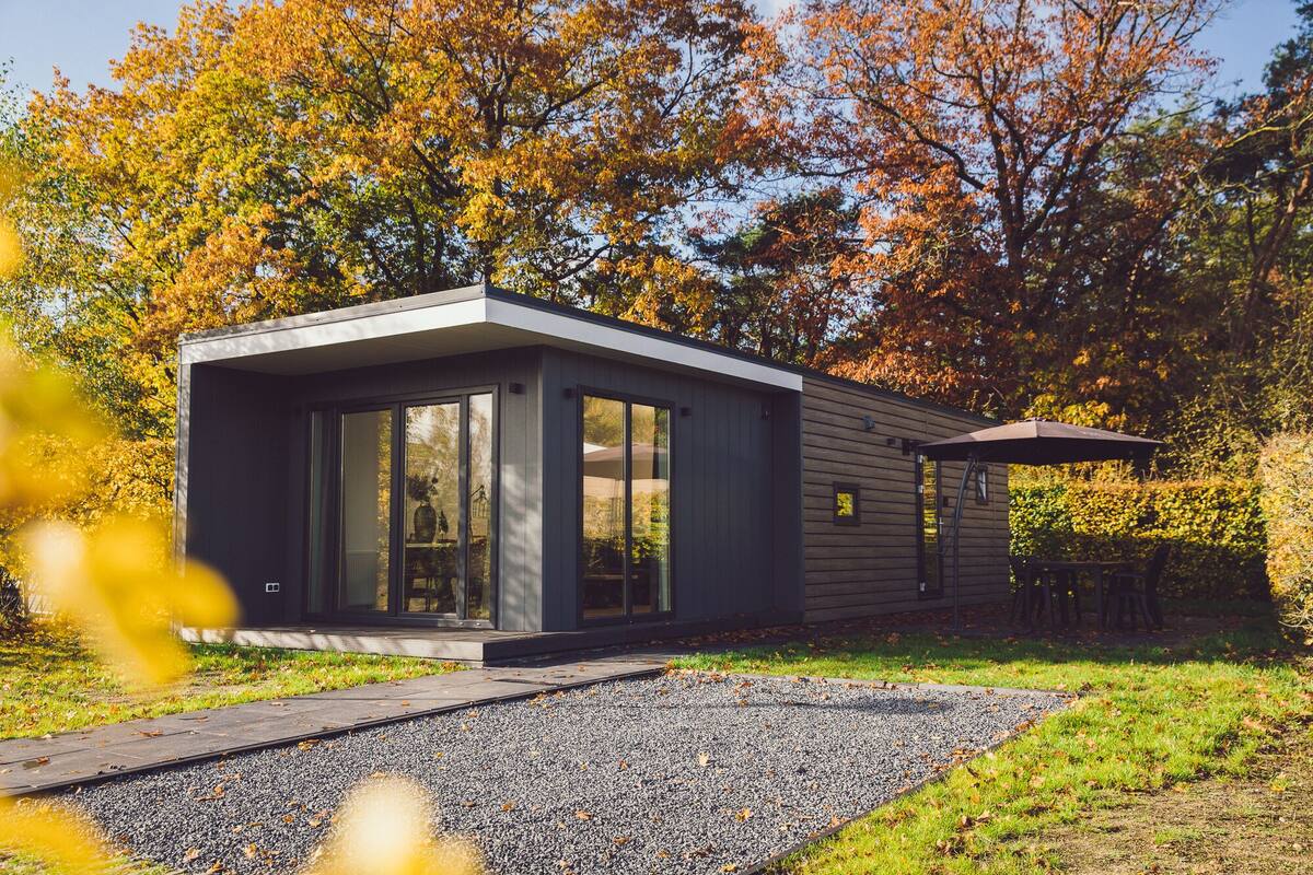 A modern, single-story house with large glass windows, a gravel driveway, and a wooden deck.