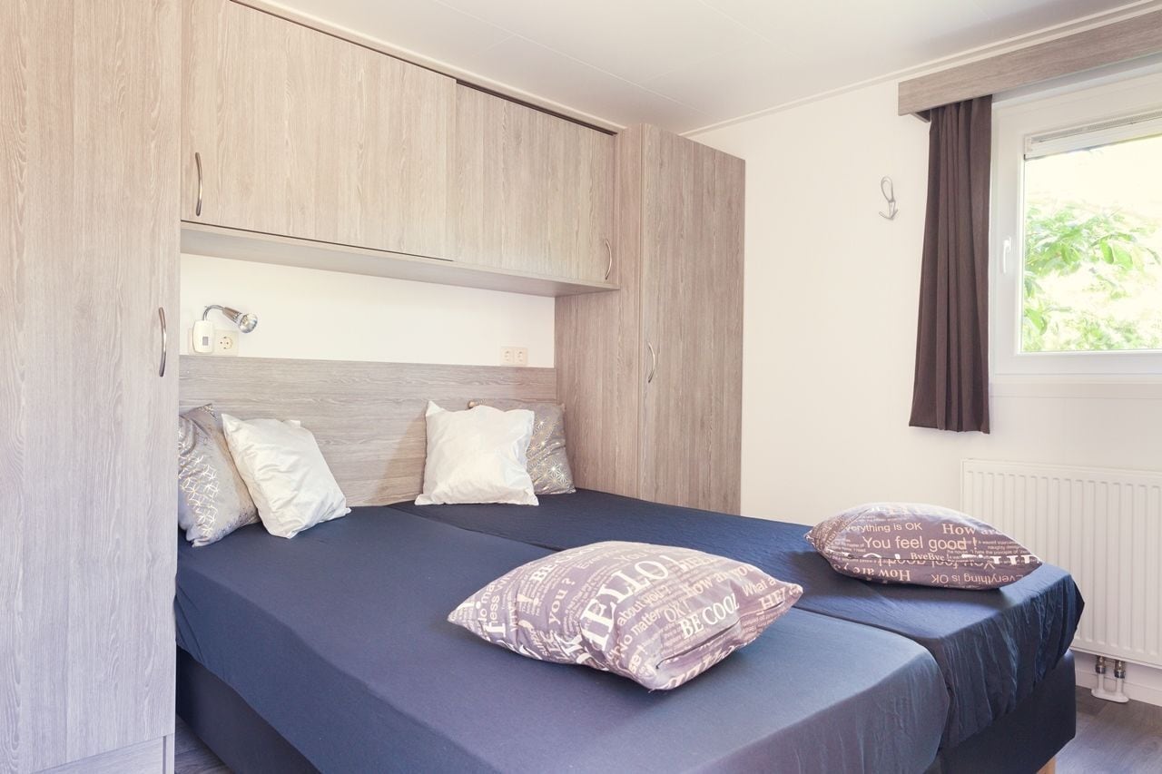 Una cama individual con cabecera, dos almohadas y una mesita de noche con lámpara.