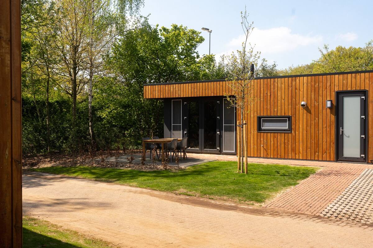 A modern building with a wooden exterior, a paved patio, and a table with chairs.