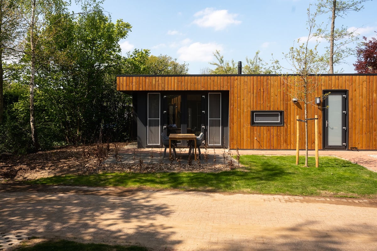 A modern house with a wooden exterior, a front door, and a small patio with a table and chairs.