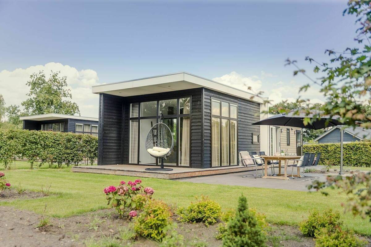 A modern house with a patio area featuring a hanging chair, a table with chairs, and a garden with flowers.