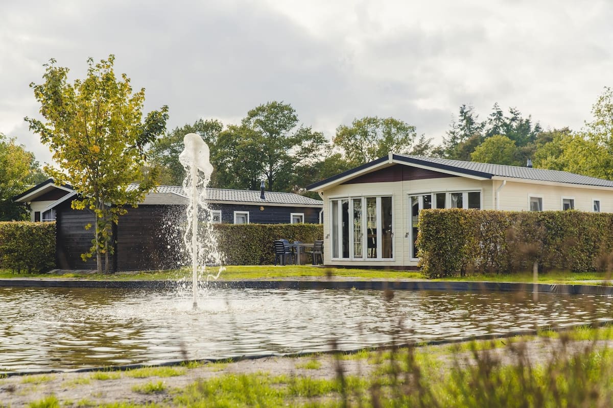 A residential area with a fountain, a house with a white exterior, and a hedge.