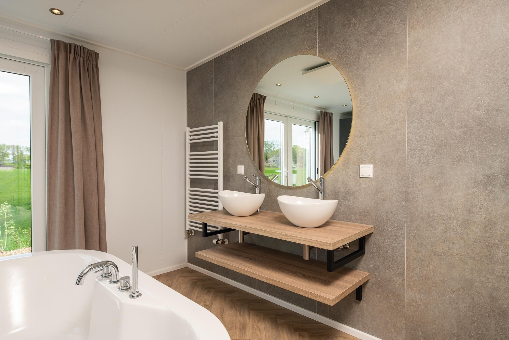 A modern bathroom with a freestanding bathtub, two vessel sinks, a towel rack, and a large mirror.