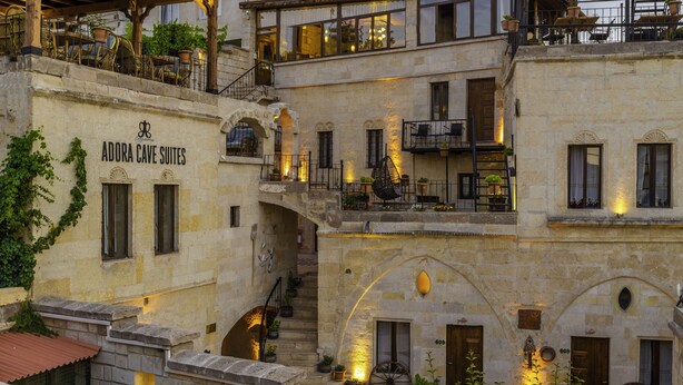 Ein mehrstöckiges Steinhaus mit Balkonen und einer Treppe, mit einem Schild, auf dem "Adora Cave Suites" steht.