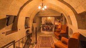 Ein gemütlicher Raum mit Steinwänden, einem Bett, einer Sitzecke mit Stühlen, einer Treppe und einem Chandelier.