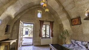 Ein Zimmer mit Steindecke, einem Holztisch, einer Couch, einem gemusterten Teppich und einem Fenster mit Vorhängen.