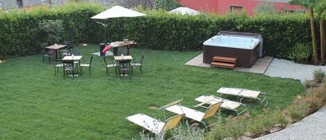 A patio area with outdoor seating, a hot tub, and a hedge.
