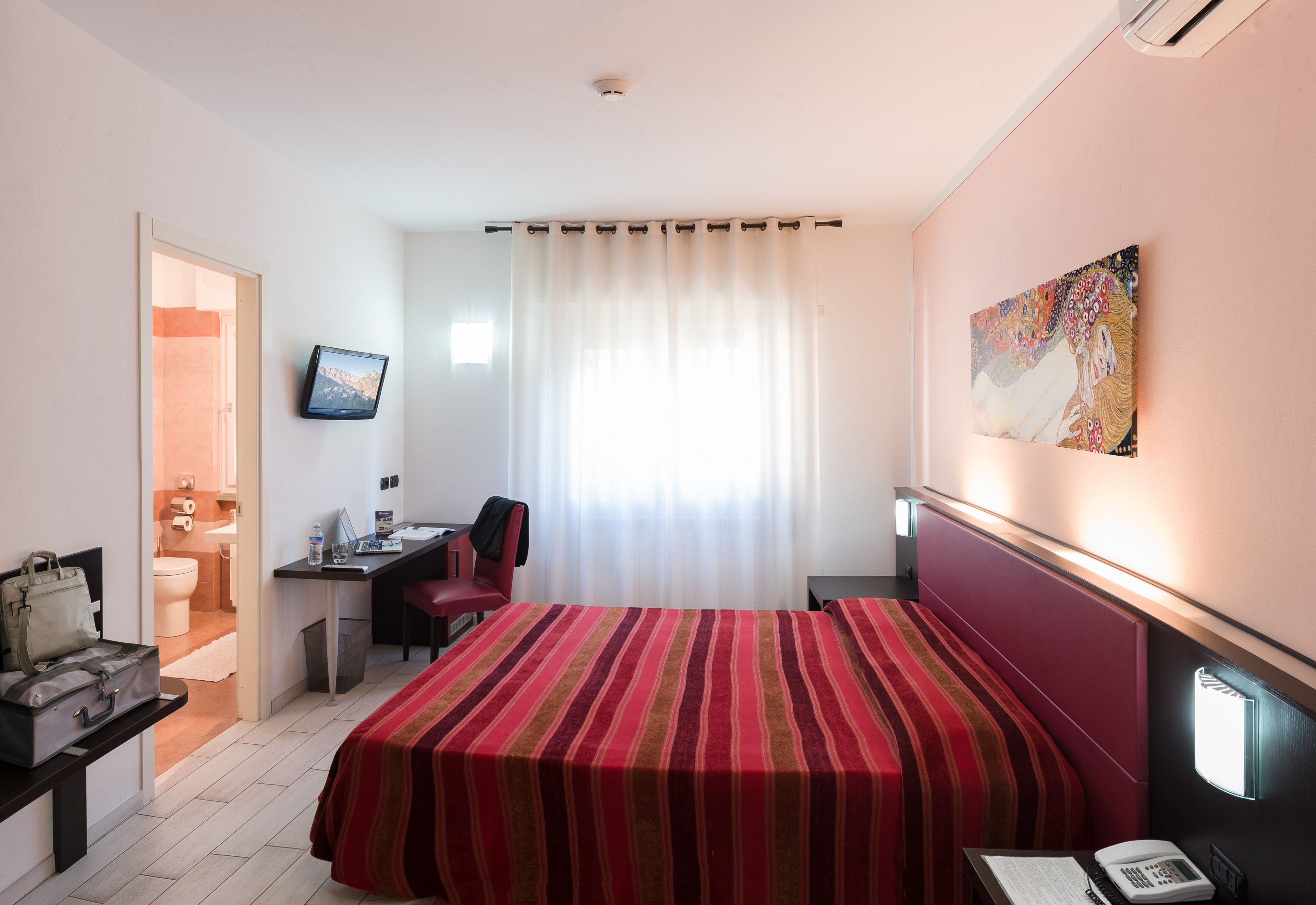 Habitación de hotel con cama, escritorio, silla y un cuadro en la pared.
