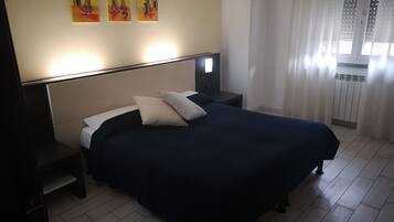 Een keurig opgemaakt bed met een donkerblauwe sprei en twee kussens, een nachtkastje met een lamp, en een muur met drie ingelijste kunstwerken.