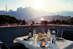 A table set for a meal with a mountain view, a bottle of wine, and a basket of bread. - Hotel Rubino (Nago-Torbole)