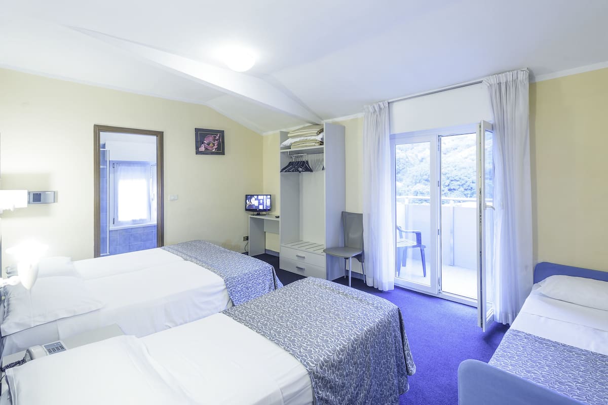A hotel room with two beds, a desk with a television, a chair, and a balcony with a view.