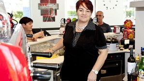Una mujer parada en la barra, con una botella de vino y copas.