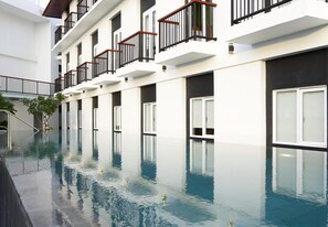 Un hotel moderno con una piscina larga, varios balcones y un diseño contemporáneo y limpio.