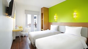 Habitación de hotel con dos camas, una mesita con una silla, un televisor fijado a la pared y una pared de acento de color verde brillante.