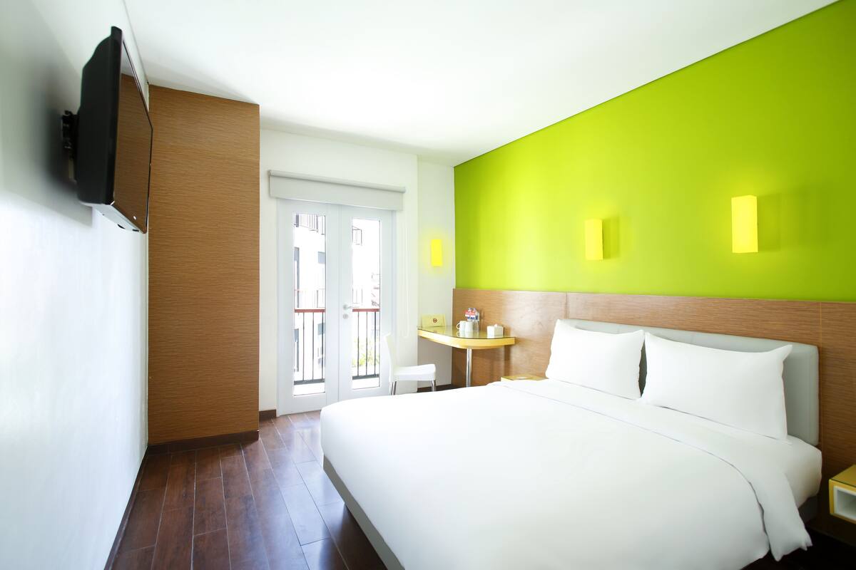 A hotel room with a bed, a desk, a chair, and a TV mounted on the wall.