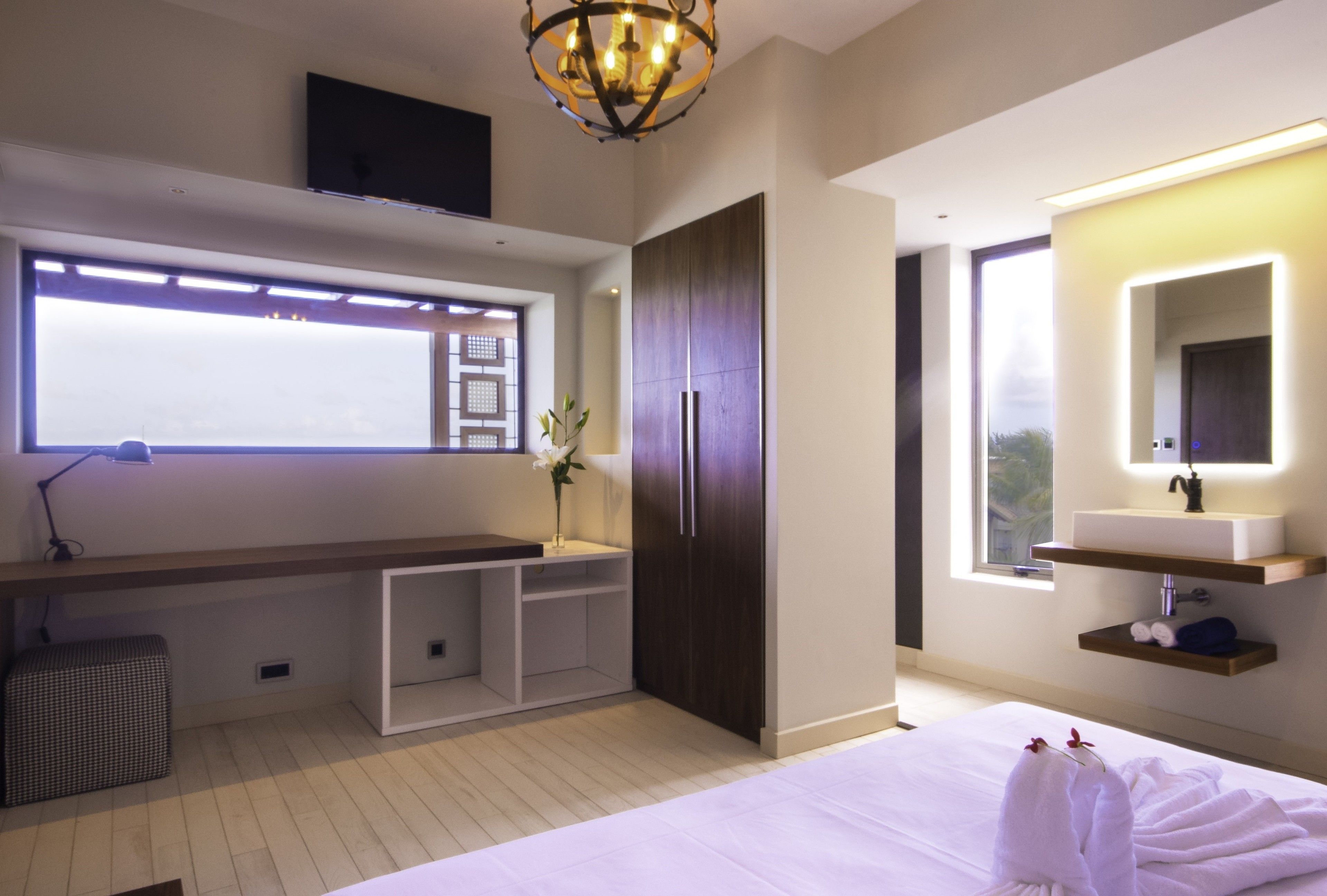 Un dormitorio moderno con una cama grande, un escritorio empotrado, un tocador con espejo y una ventana con vistas.
