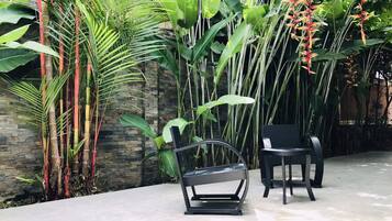 A patio area with a black exercise bike, two black chairs, and lush tropical plants.
