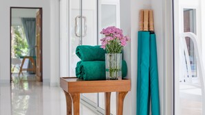 Una mesa de madera con una toalla verde, un jarrón de flores rosas y un par de toallas color turquesa apoyadas contra un vidrio.