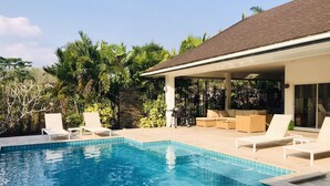 Una piscina con sillas de descanso y una zona de estar techada.
