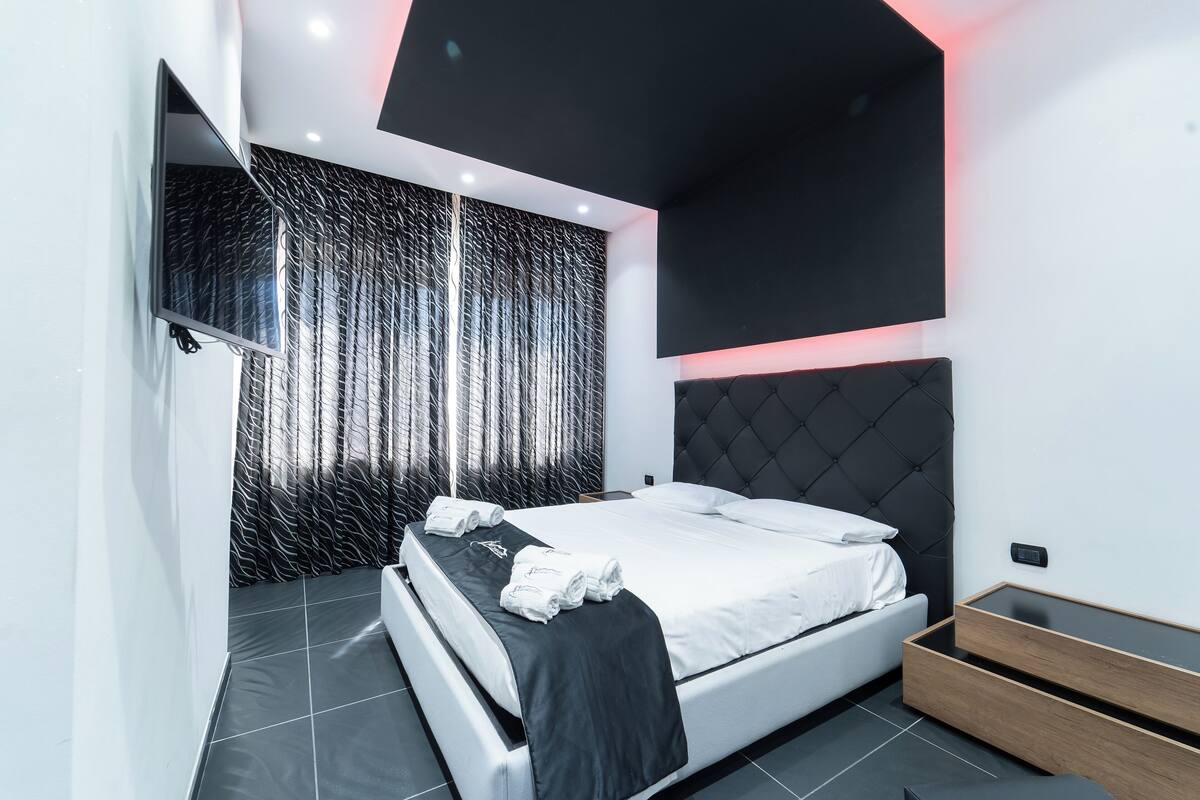 Een moderne slaapkamer met een bed, nachtkastje en een tv aan de muur.