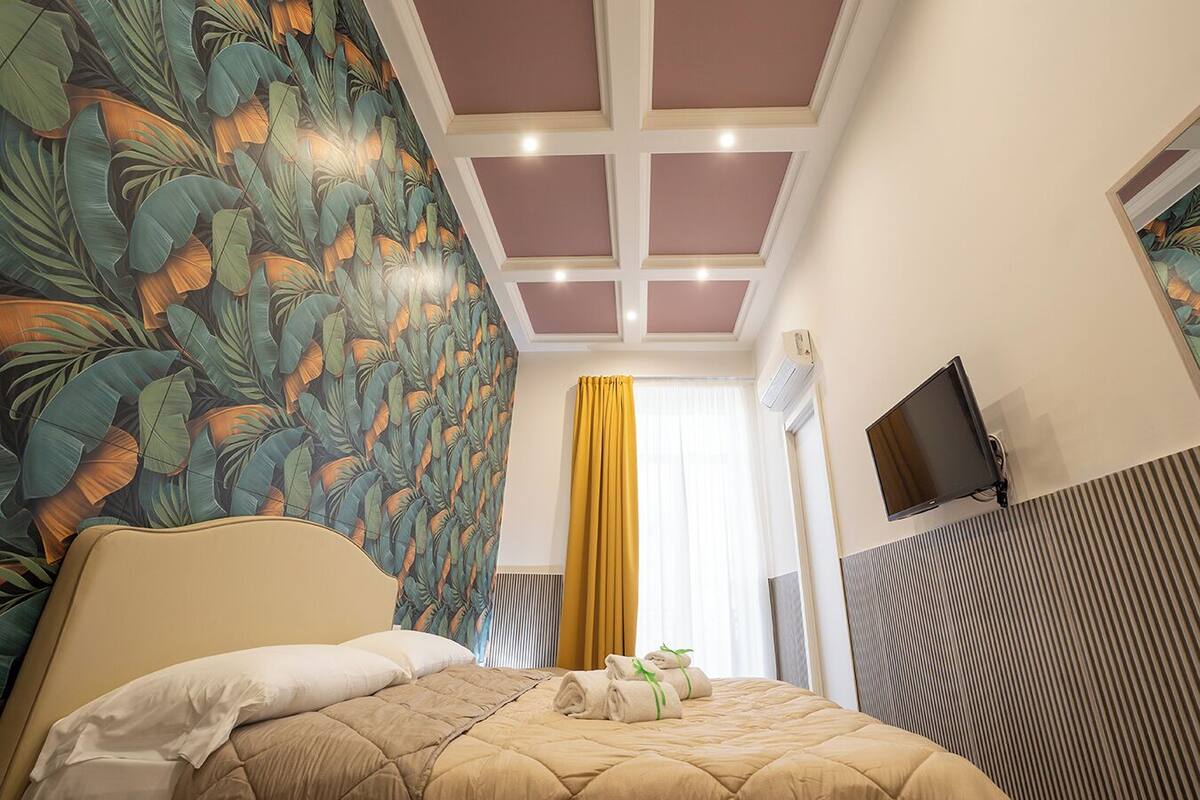 Een hotelkamer met een bed, een televisie, een plafond met inbouwverlichting en een raam met gordijnen.