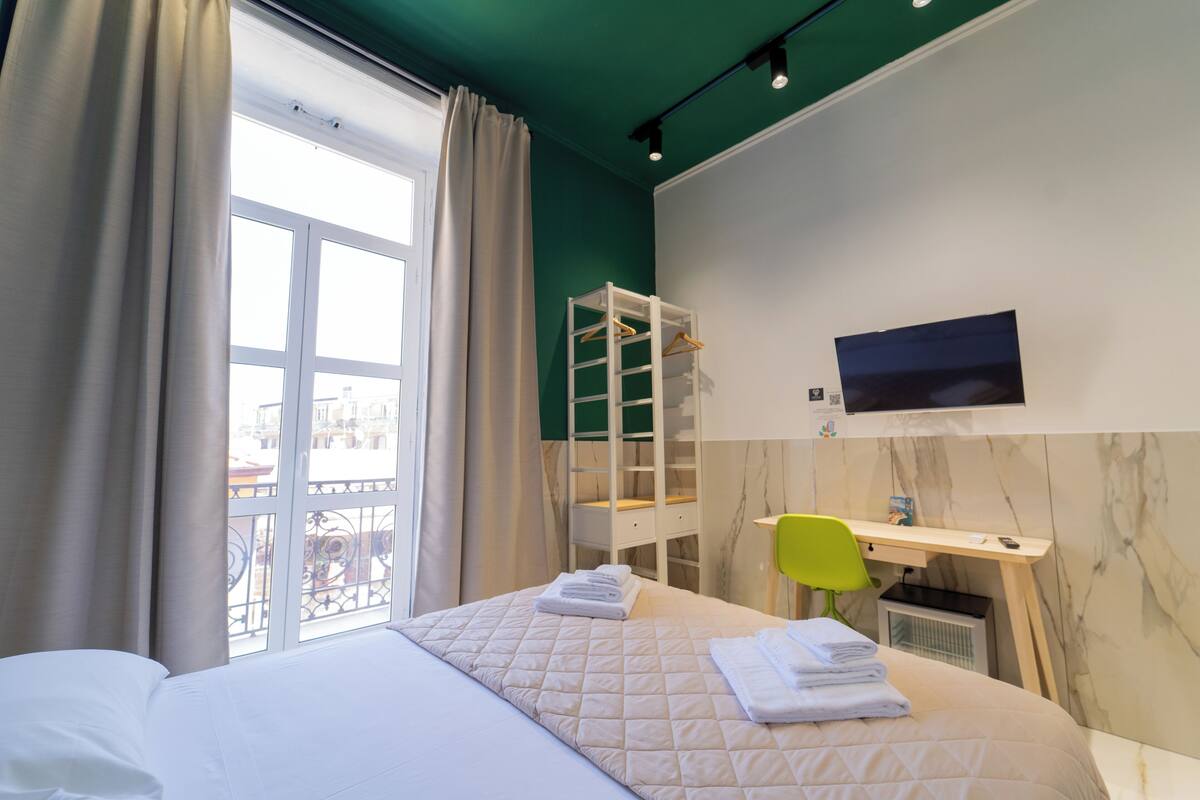 Een hotelkamer met een bed, een bureau, een stoel, een televisie en een raam met gordijnen.