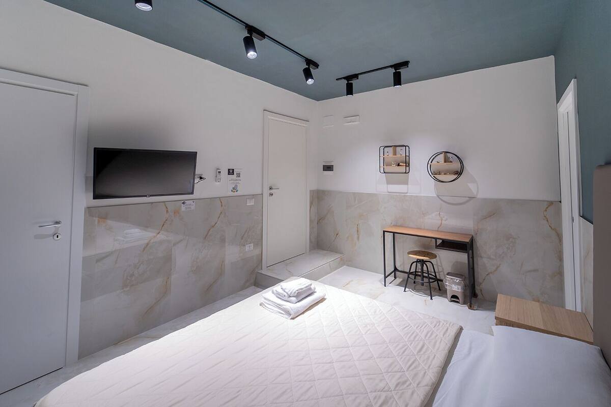 Een moderne slaapkamer met een bed, een bureau en een televisie aan de muur.