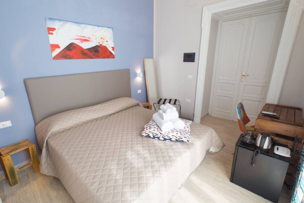 Een slaapkamer met een bed, een schilderij aan de muur, een deur en een klein tafeltje met spullen erop.