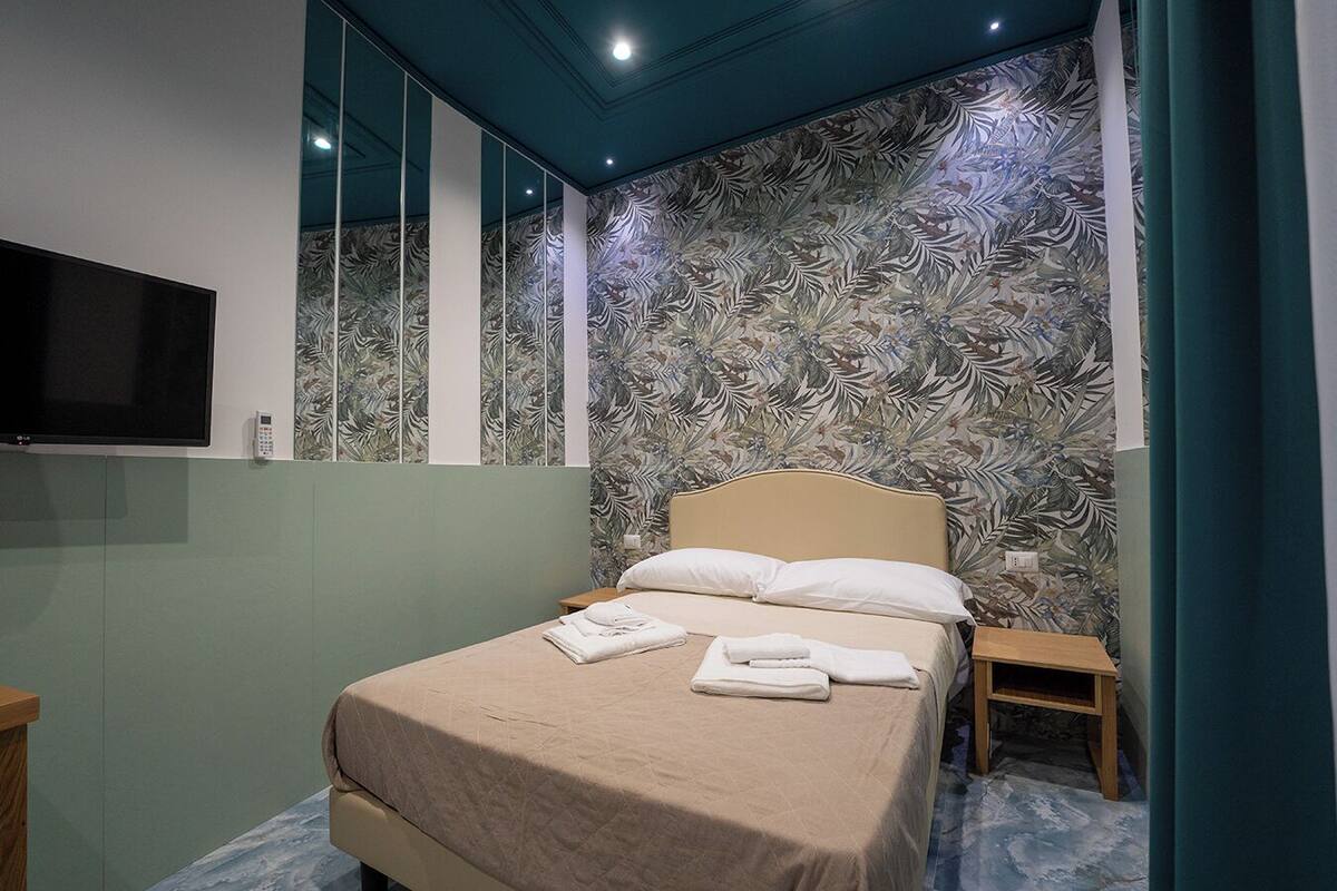 Een slaapkamer met een bed, een aan de muur bevestigde televisie en behang met een patroon.
