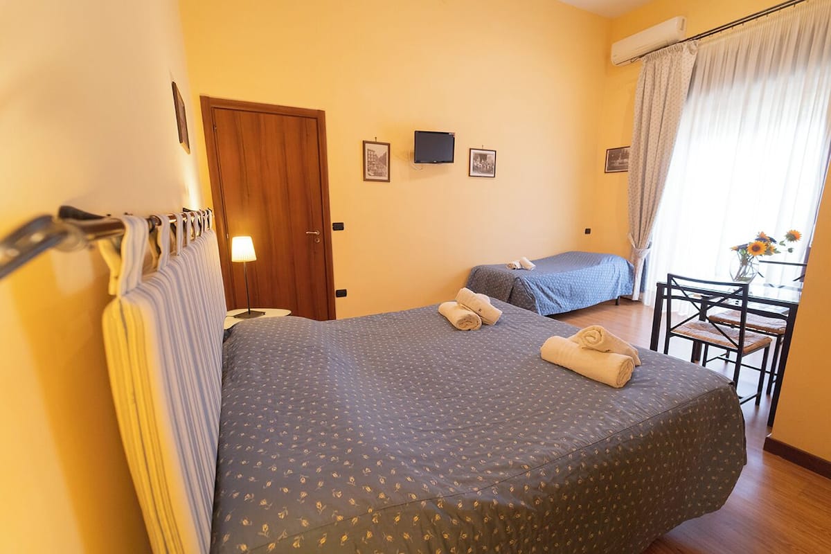 Hotelkamer met twee bedden, een bureau met stoel, een raam met gordijnen en een tv aan de muur.