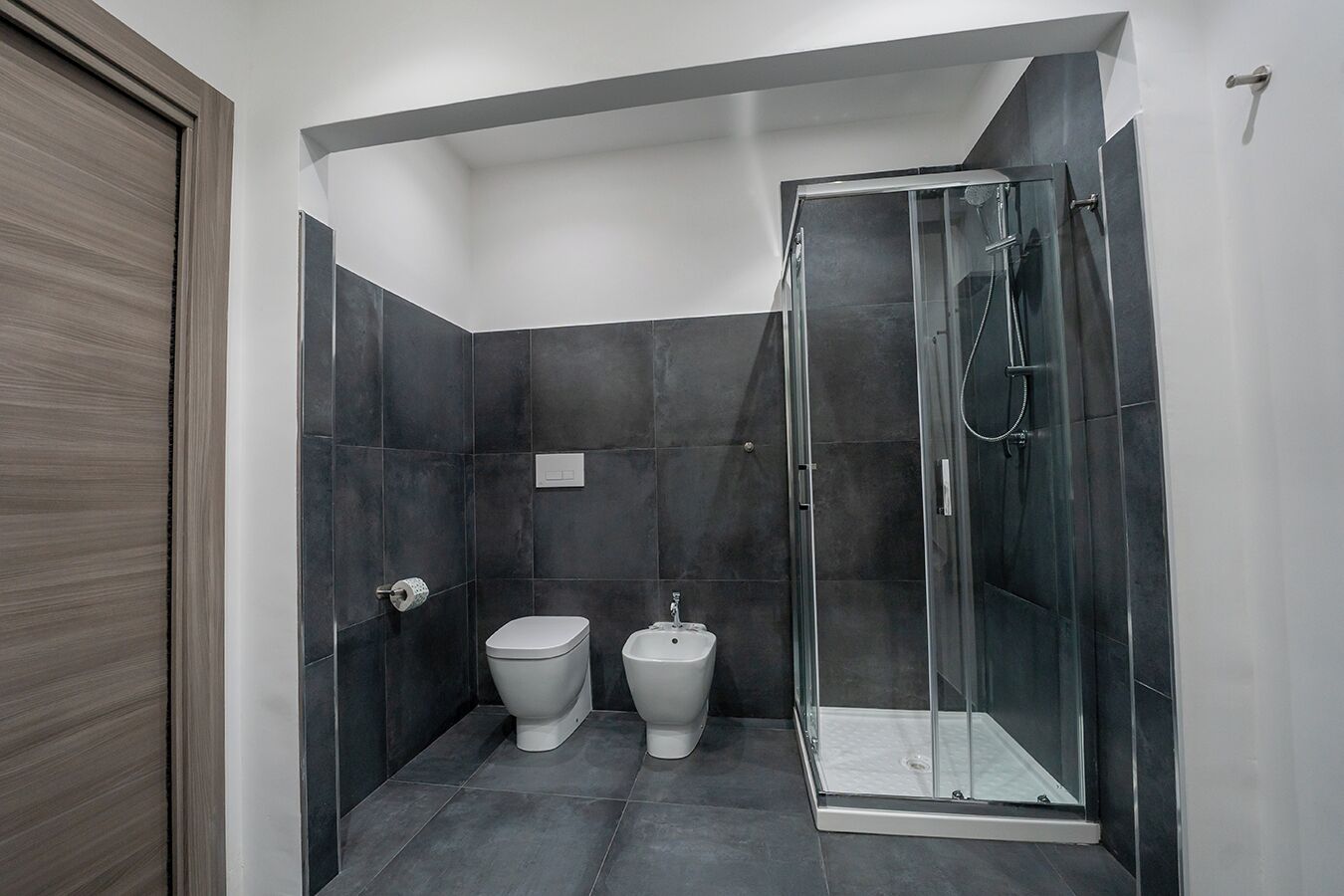 Ein modernes Badezimmer mit dunklen Fliesen, einer Glasdusche und einer Toilette.