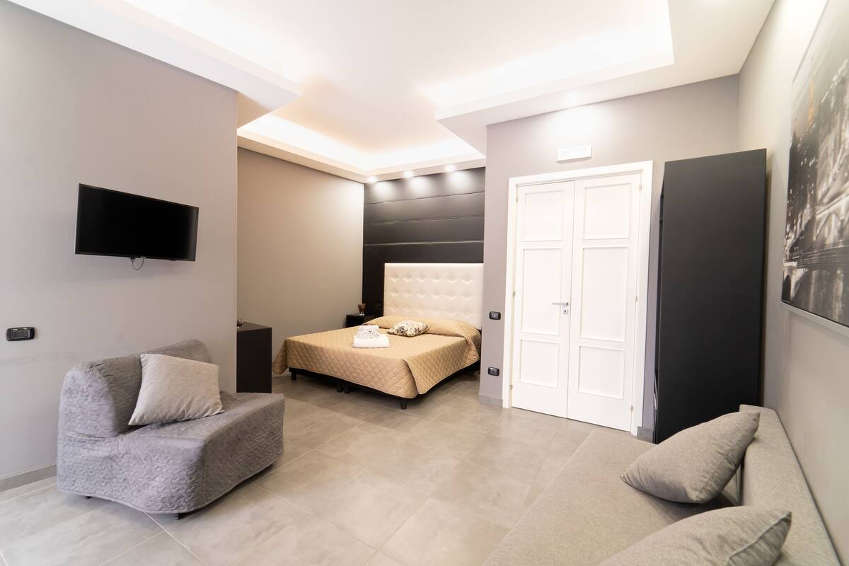 Een moderne slaapkamer met een bed, een bank, een televisie en een deur.