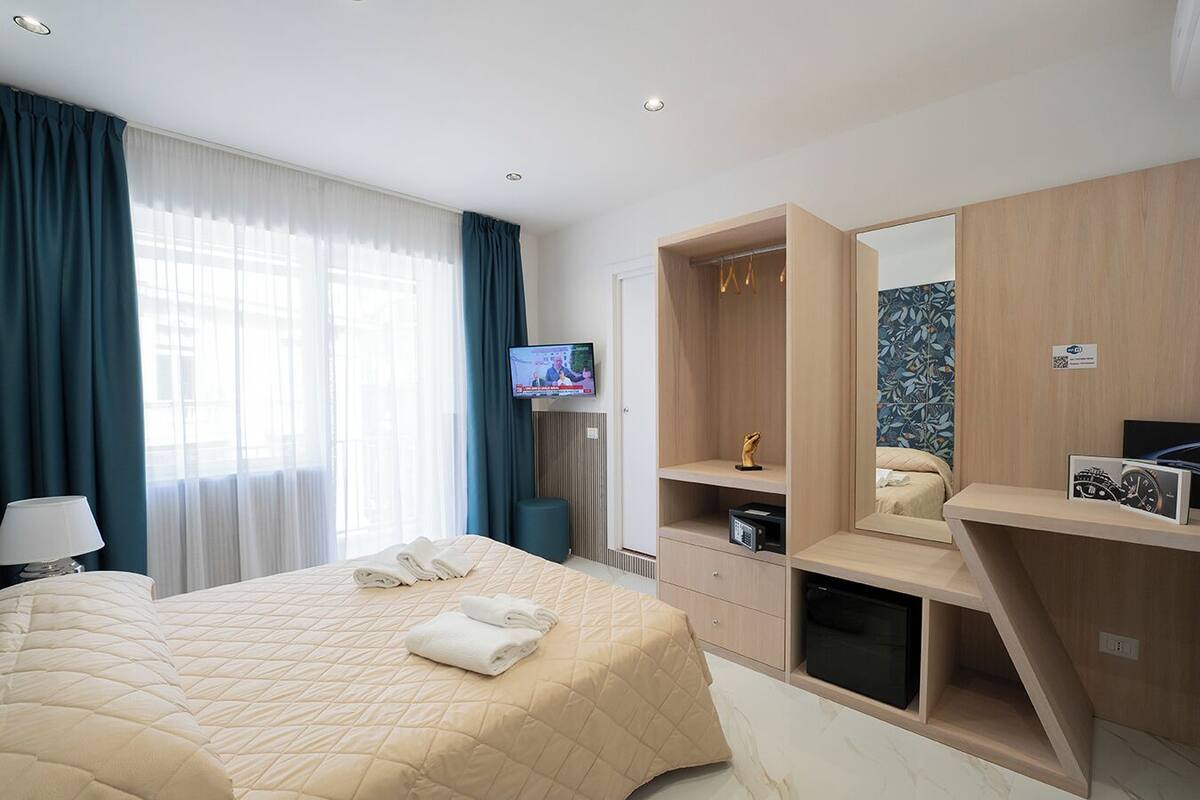 Een hotelkamer met een groot bed, een aan de muur bevestigde televisie, een garderobe en een spiegel.