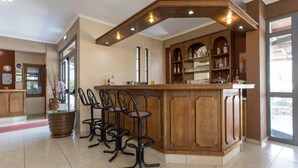 A bar area with a wooden counter, bar stools, and a shelf with bottles and glasses.