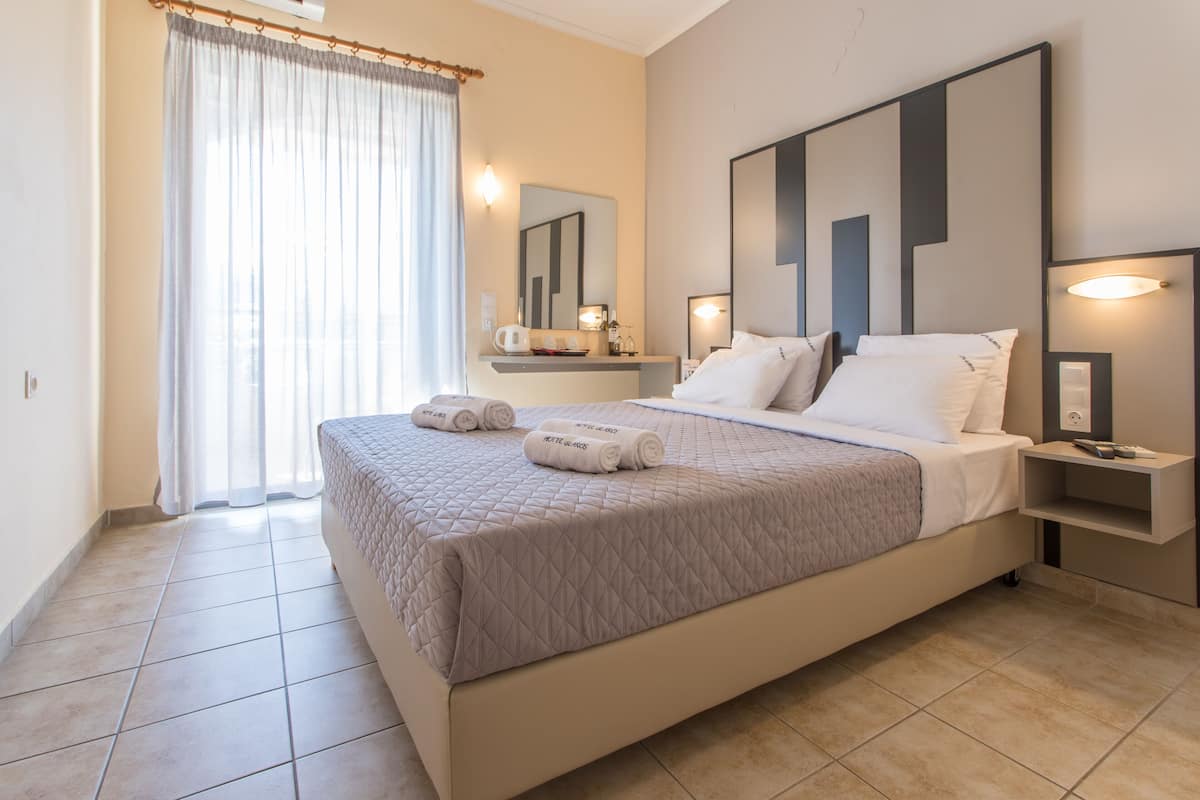 Een moderne hotelkamer met een groot bed, een nachtkastje, een spiegel en een raam met gordijnen.