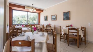 A dining area with multiple tables and chairs, large windows with a view of greenery, and wall-mounted artwork.