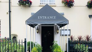 Entrada de un hotel con alfombra roja, una marquesina que dice 'ENTRANCE' y plantas en macetas a cada lado.