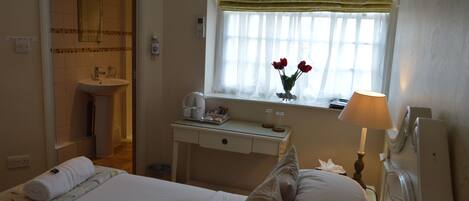 A hotel room with a bed, a bedside table with a lamp, a window with a view of the outside, and a bathroom with a sink and mirror.