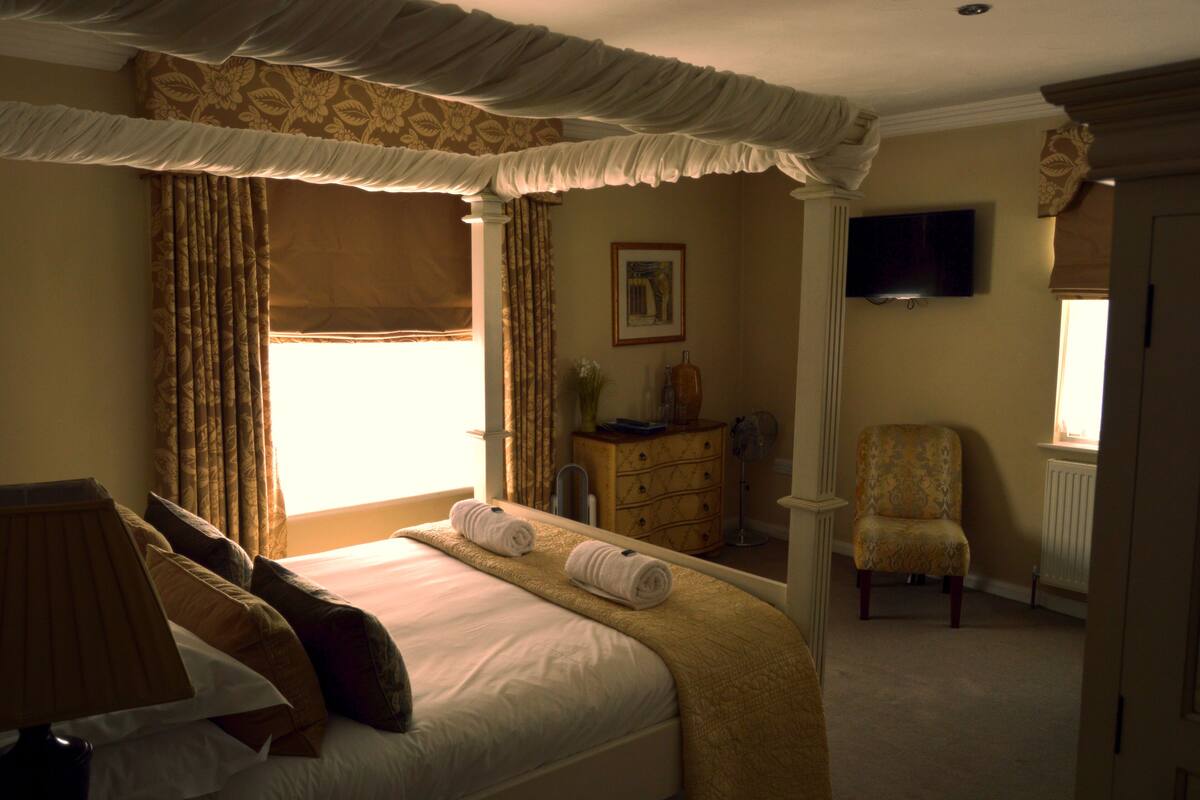 Una habitación de hotel con una cama grande, un aparador, una silla y un televisor en la pared.