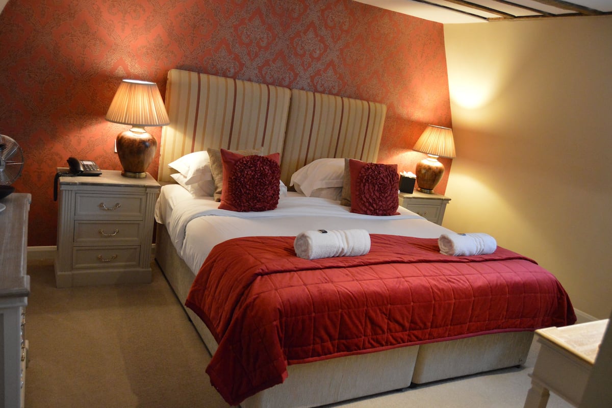Una habitación de hotel con una cama grande, dos mesitas de noche con lámparas, un teléfono y un aparador.