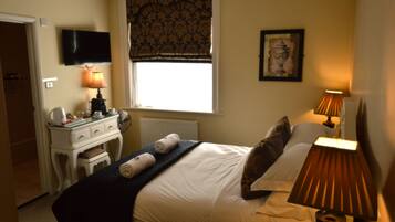 A hotel room with a bed, bedside lamps, a dresser, a television, a window with a valance, and a framed picture on the wall.